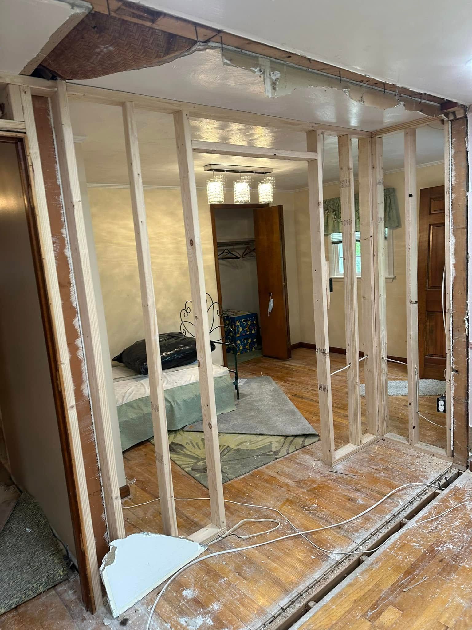 Exposed wooden wall studs in a room under renovation, with drywall and debris on the floor.