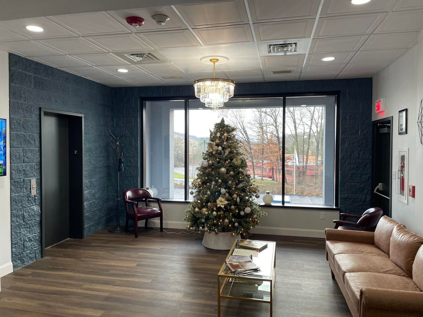 Lobby with Christmas tree, tan couch, chandelier, and large window in a modern office waiting area