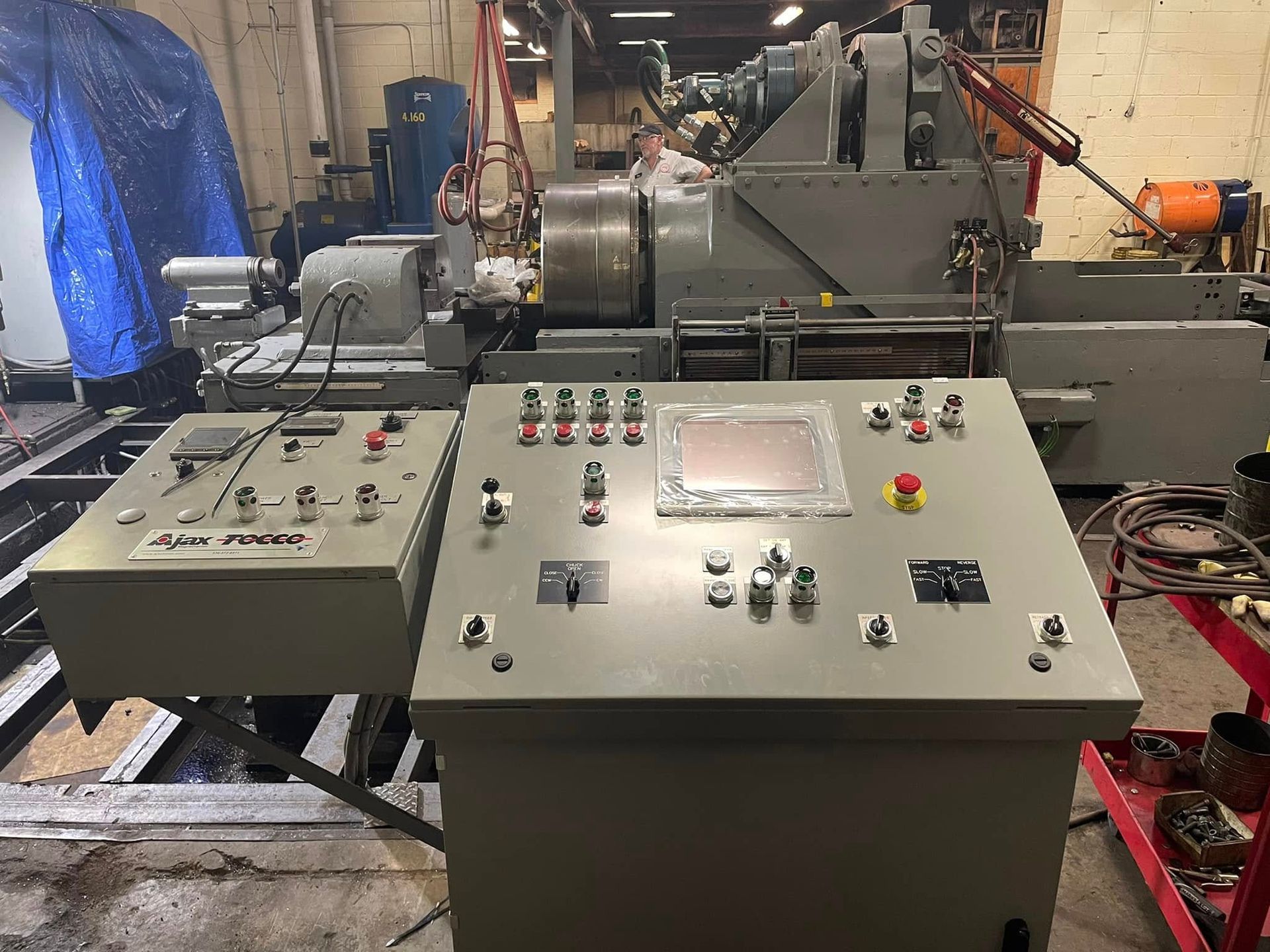 Industrial control panels beside a large machine in a workshop, with buttons, dials, and an emergency stop.