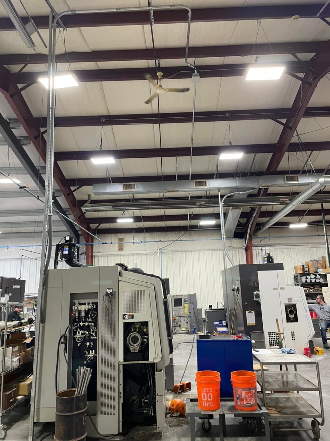 Industrial workshop with large machines, overhead lights, and orange buckets on the floor