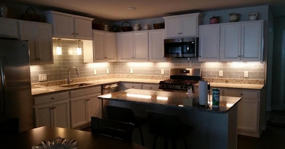 Dimly lit modern kitchen with white cabinets, stainless appliances, and a large island.