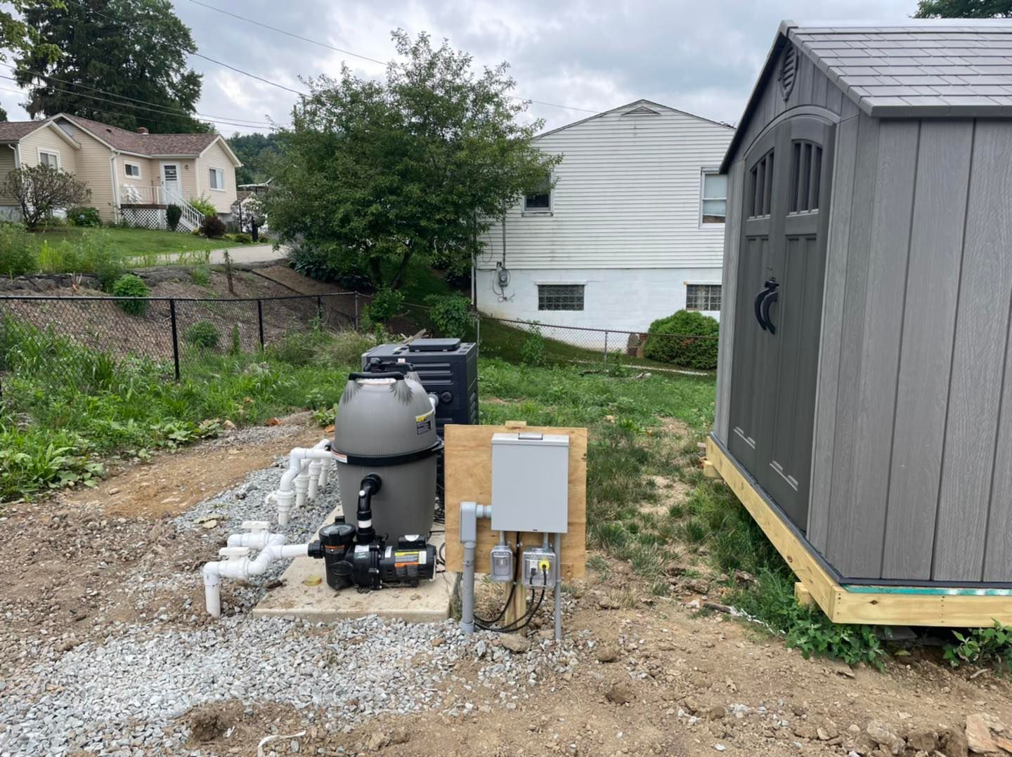Backyard with a gray grill, utility box, and a dark garden shed on gravel.