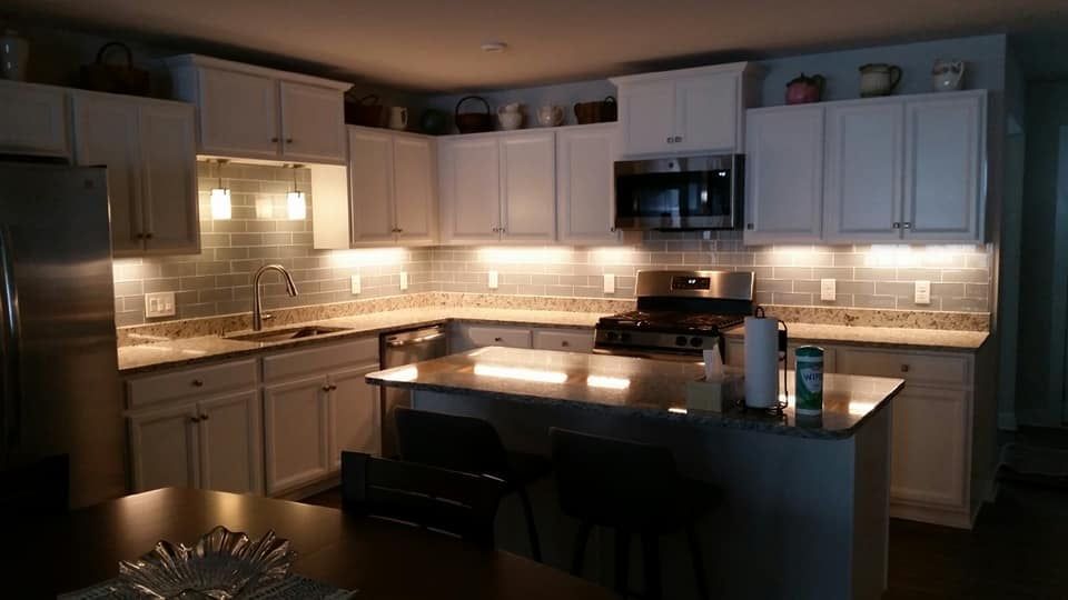Dim modern kitchen with white cabinets, warm under-cabinet lighting, and a dark island countertop.
