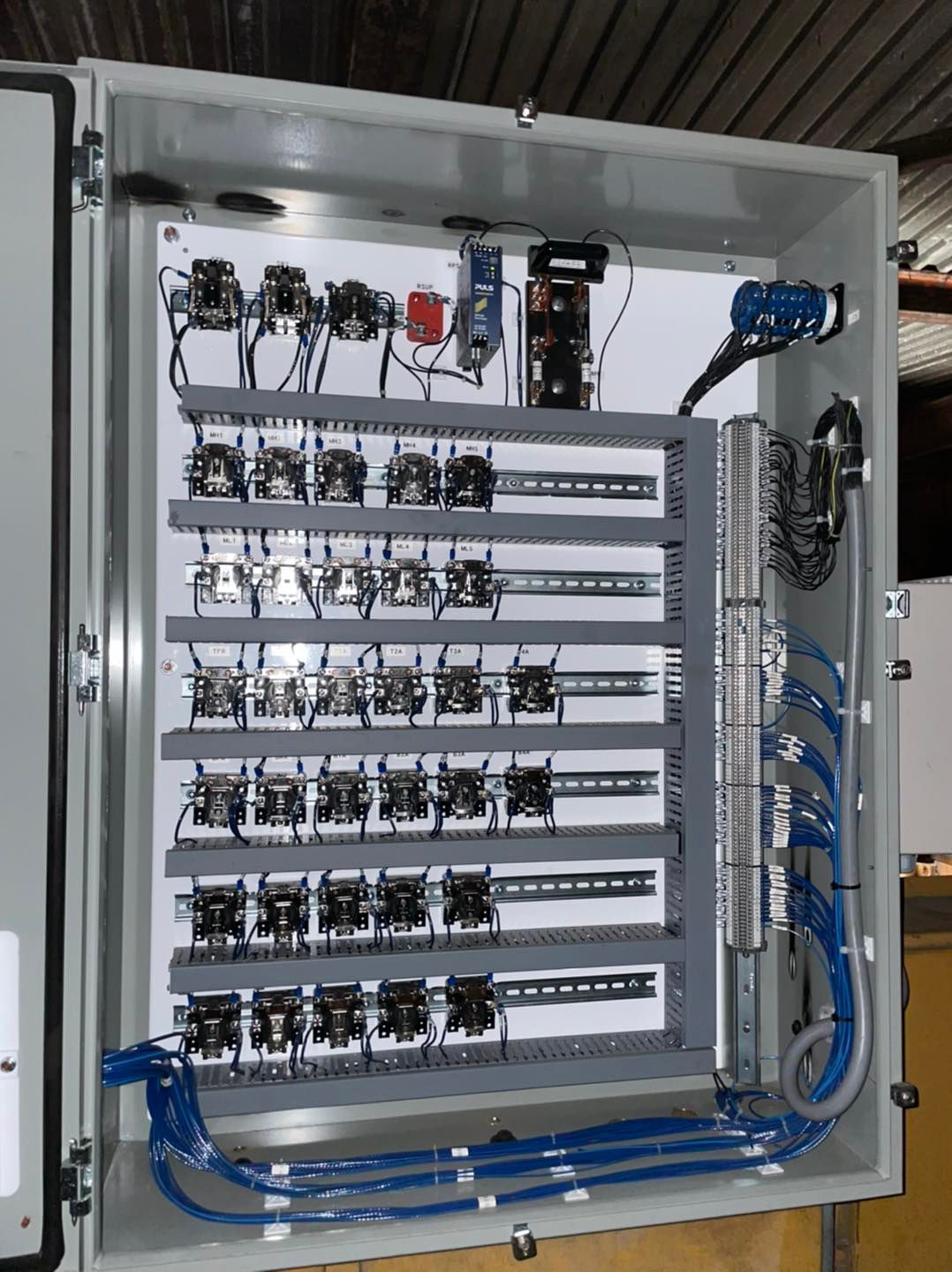 Open electrical control cabinet with wiring, relays, and blue hoses mounted inside.