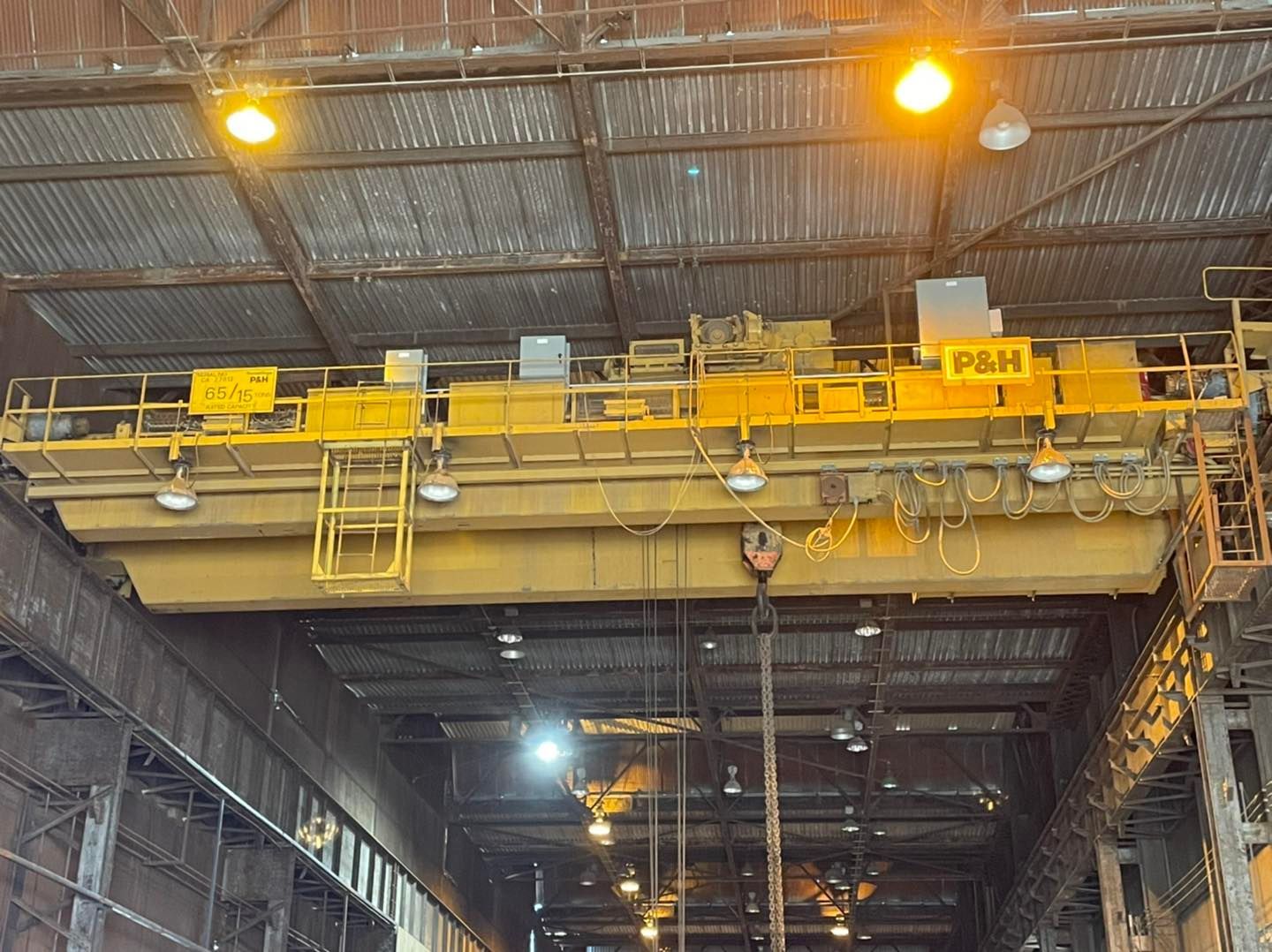Yellow overhead crane inside a large industrial warehouse with bright ceiling lights