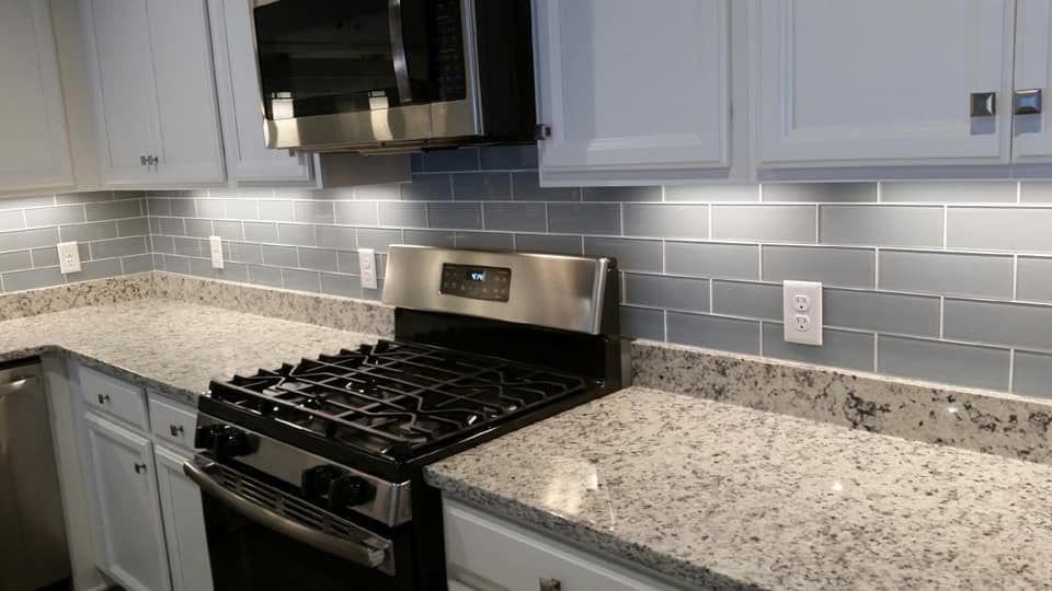 Modern kitchen with gray cabinets, speckled countertops, stainless stove, and gray subway tile backsplash