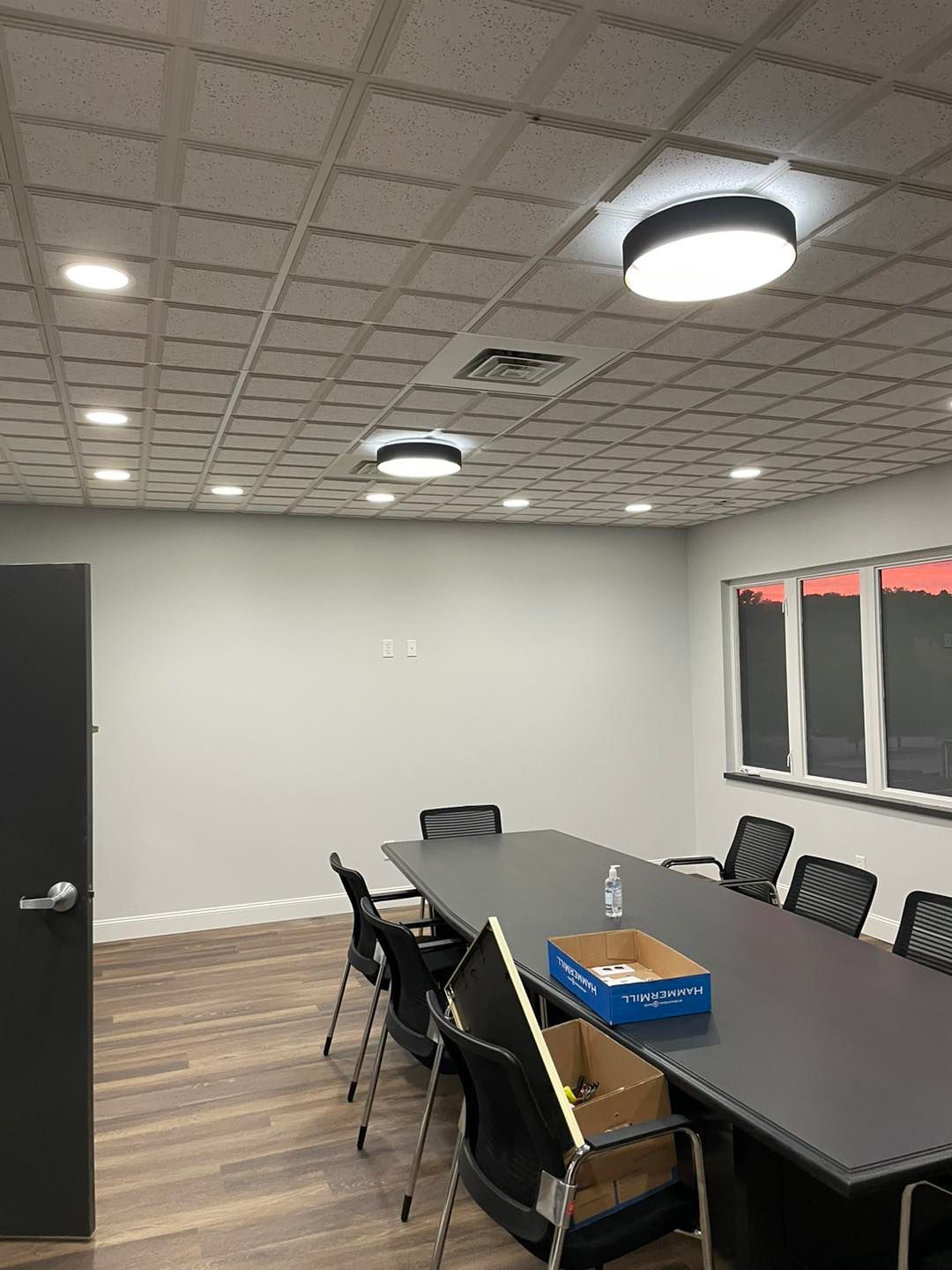 Empty conference room with long dark table, black chairs, wall windows, and ceiling lights
