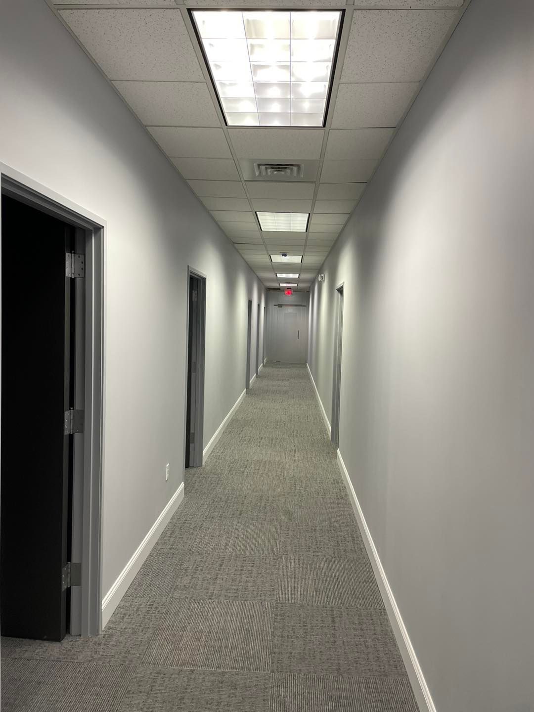 Long office hallway with gray walls, carpet, and fluorescent ceiling lights