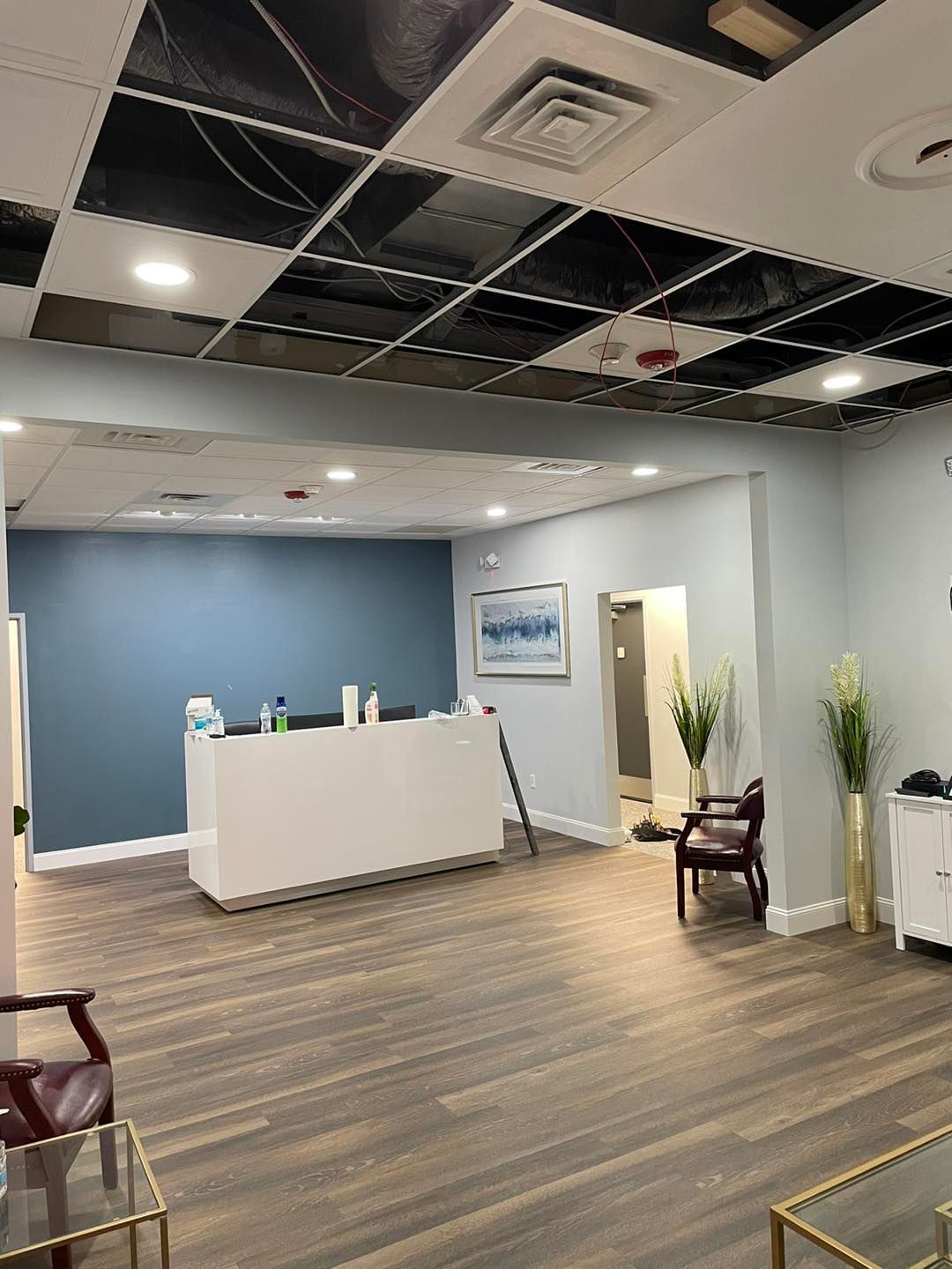 Empty modern lobby with white reception desk, blue accent wall, and chairs under a partially exposed ceiling.