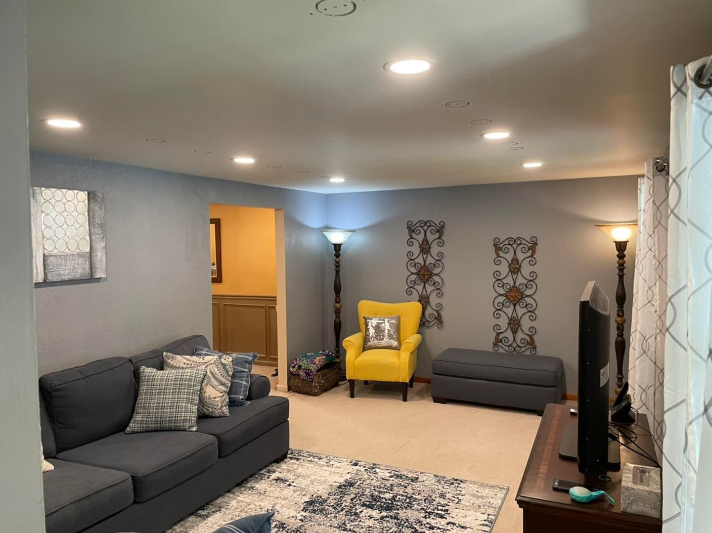 Living room with gray sofas, yellow chair, wall art, and recessed ceiling lights
