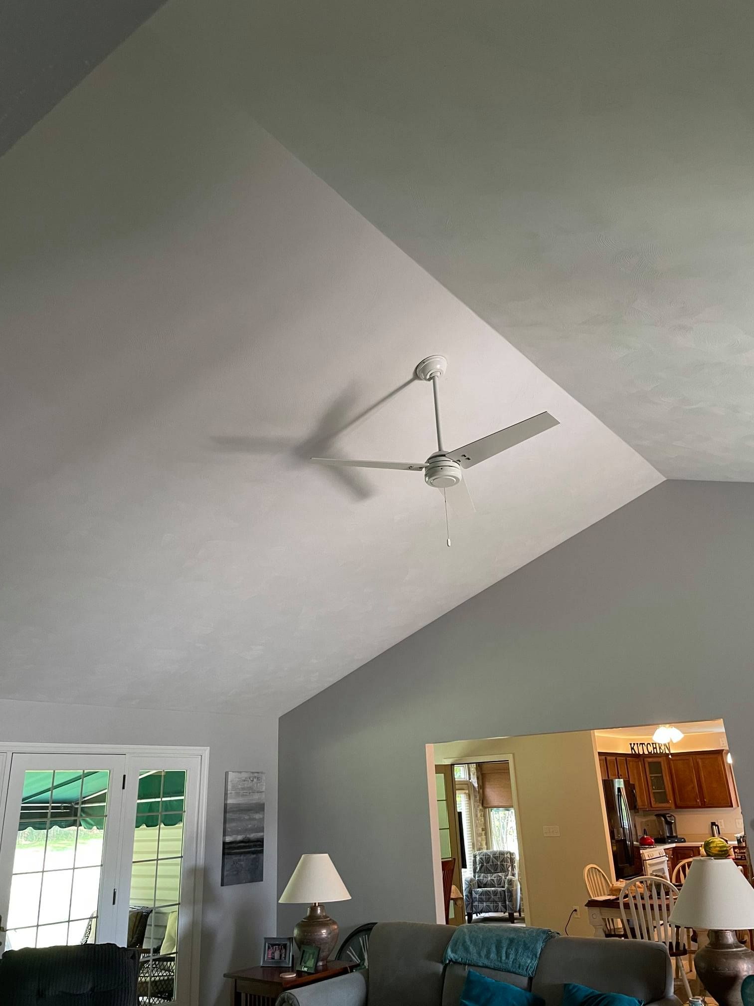Living room with vaulted ceiling, white ceiling fan, and open kitchen area below.