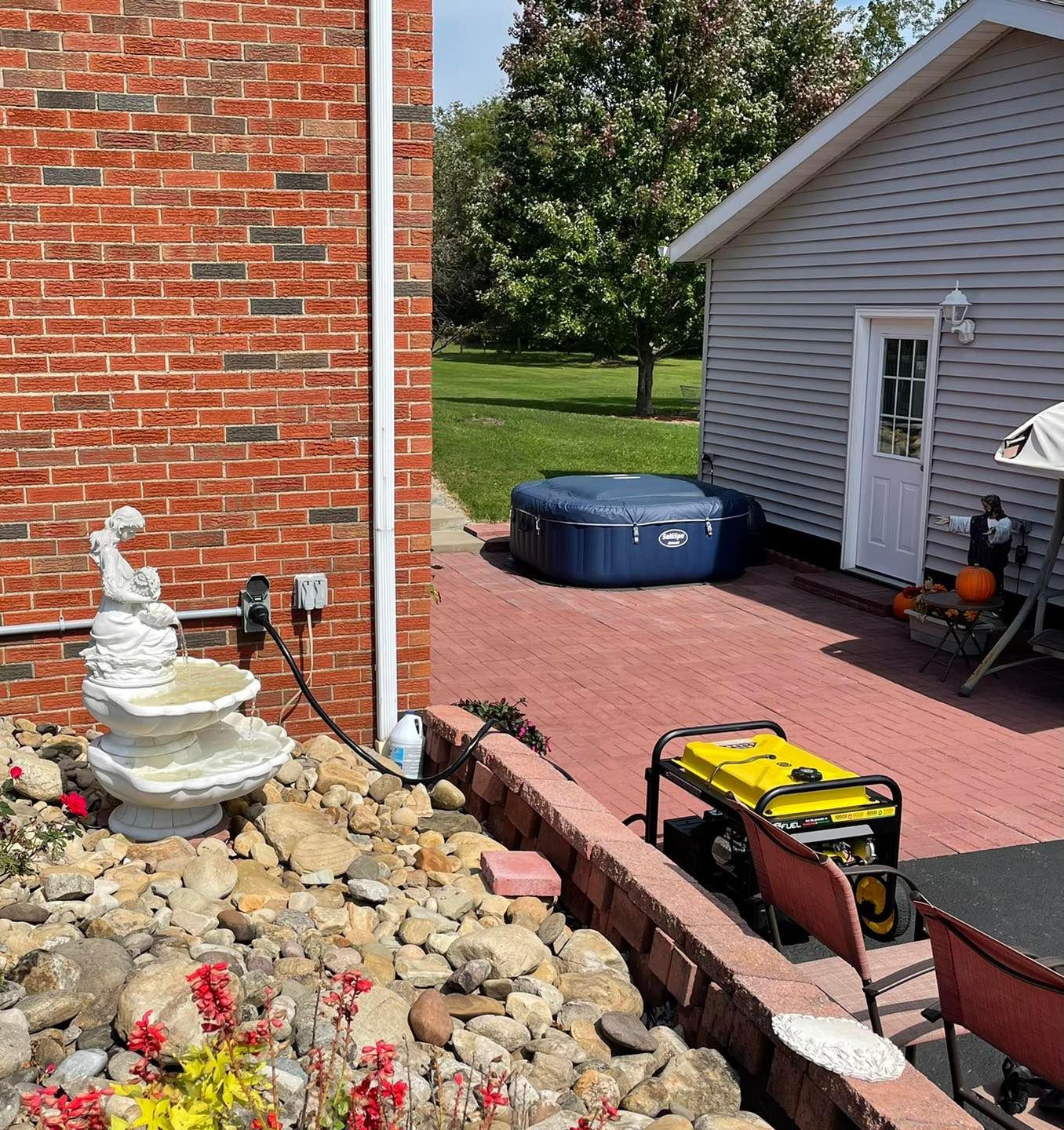 Backyard patio with brick wall, small fountain, hot tub, and red paver walkway beside a garage