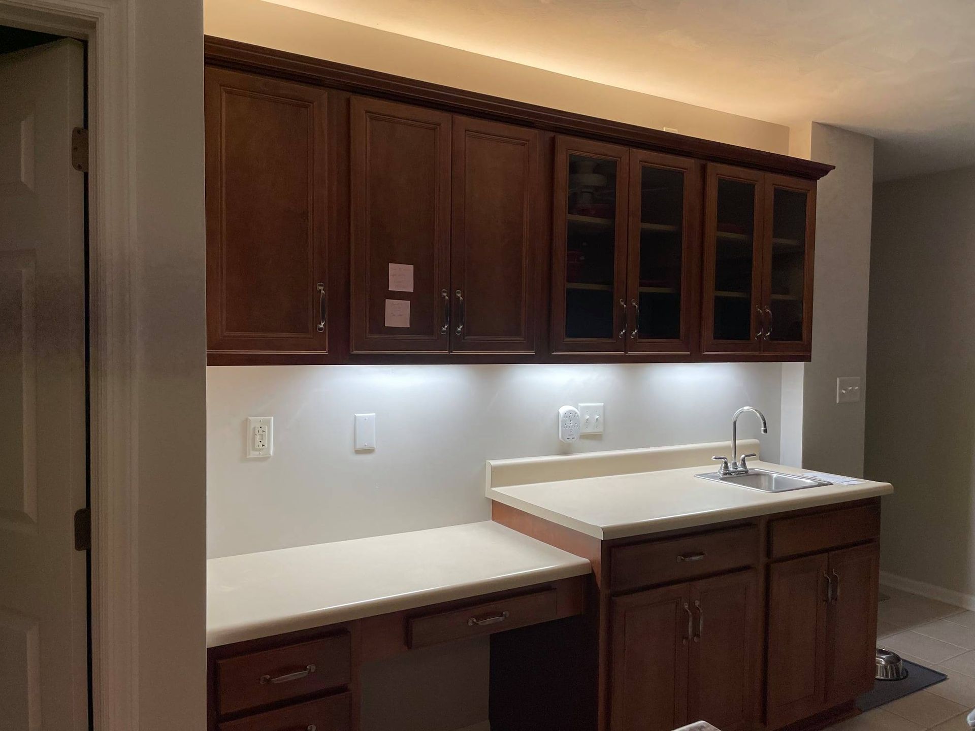 Kitchen with dark wood cabinets, light countertops, and a sink under under-cabinet lighting.