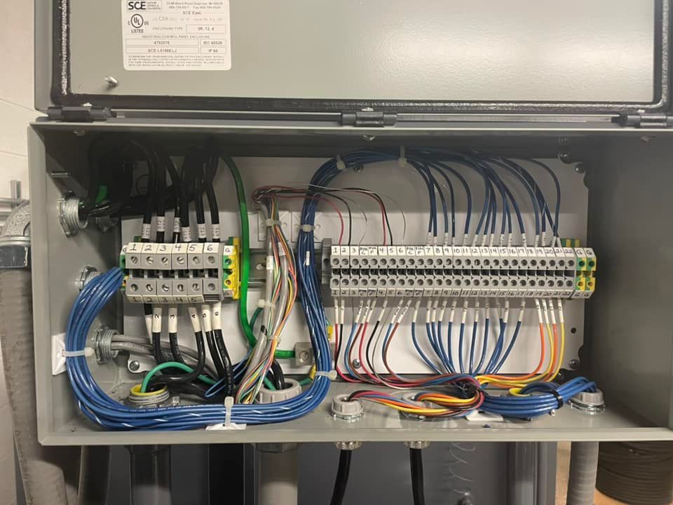 Open electrical control cabinet with wiring, relays, terminals, and blue cables inside.