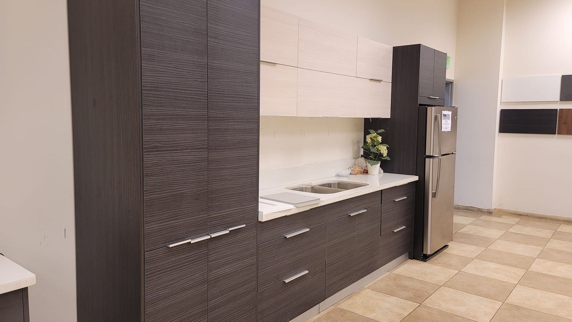 Modern kitchen with dark brown and cream-colored cabinets, stainless steel refrigerator, and white countertop. Beige tiled floor.