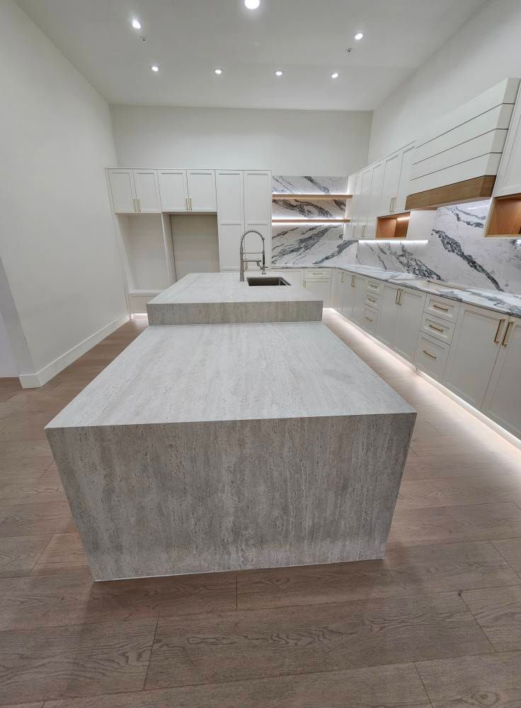 Modern kitchen with a large, light wood island and white cabinetry with marble countertops. Wood flooring and recessed lighting.