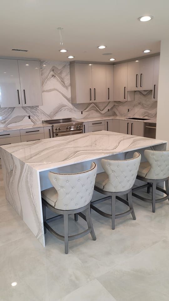 Modern kitchen with a large island featuring a marble countertop, seating, and matching cabinetry, with a stainless steel range.