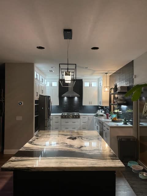 Modern kitchen with a marble countertop island, white cabinets, black accents, and hanging light fixtures.