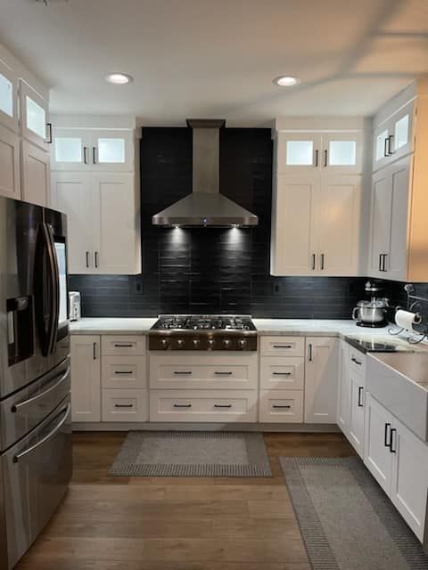 White kitchen with stainless steel appliances and a black backsplash. Cabinets surround a stovetop and range hood.
