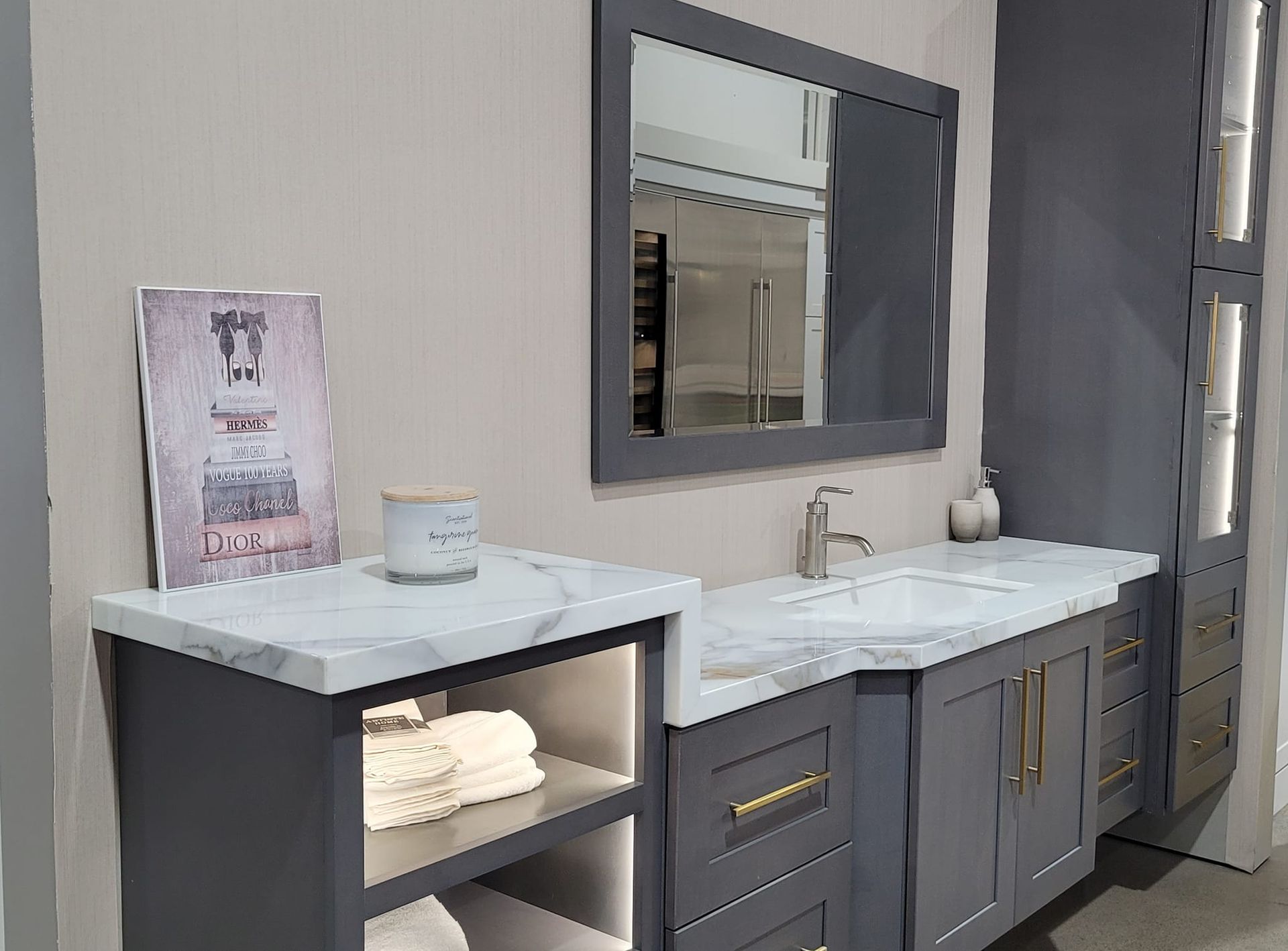 Bathroom vanity with gray cabinets, marble countertop, rectangular mirror, and open shelf, featuring a candle and artwork.