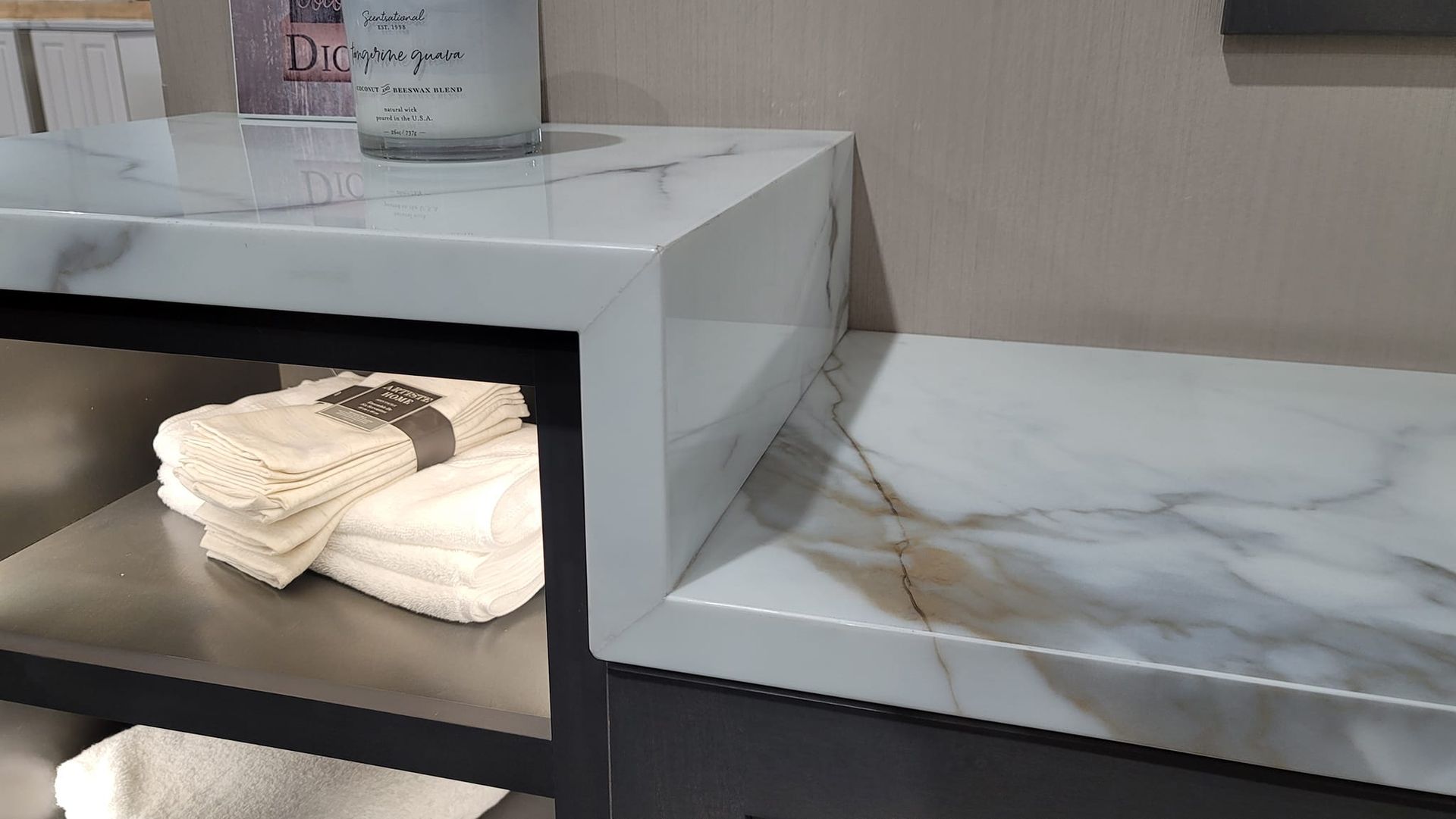 A close-up of a modern vanity with a white marble countertop. Below, a metal shelf holds folded white towels.