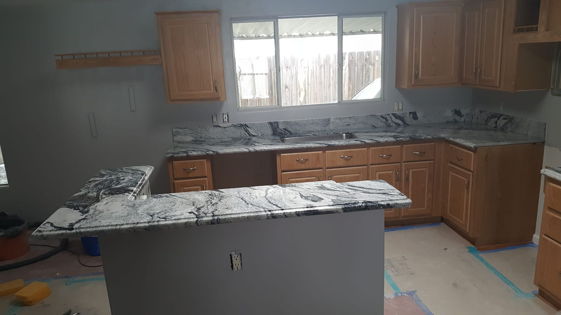 Kitchen remodel with granite countertops and light wood cabinets. Grey walls, a window, and an island with a breakfast bar are visible.