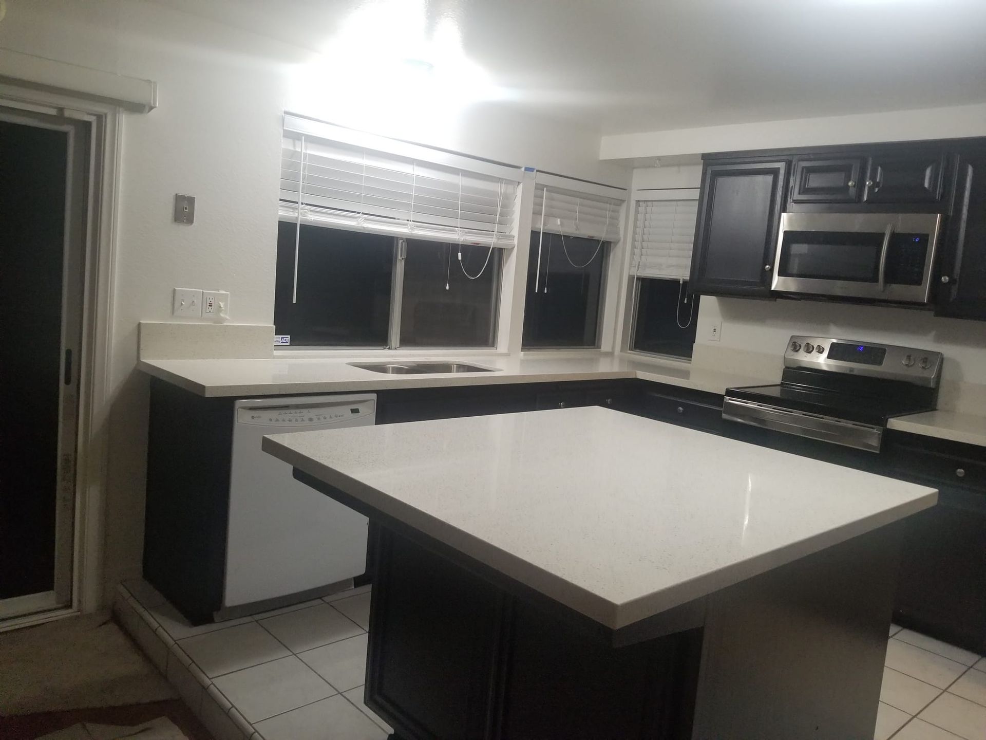 Kitchen with black cabinets, white countertops, and a large island. Stainless steel appliances.