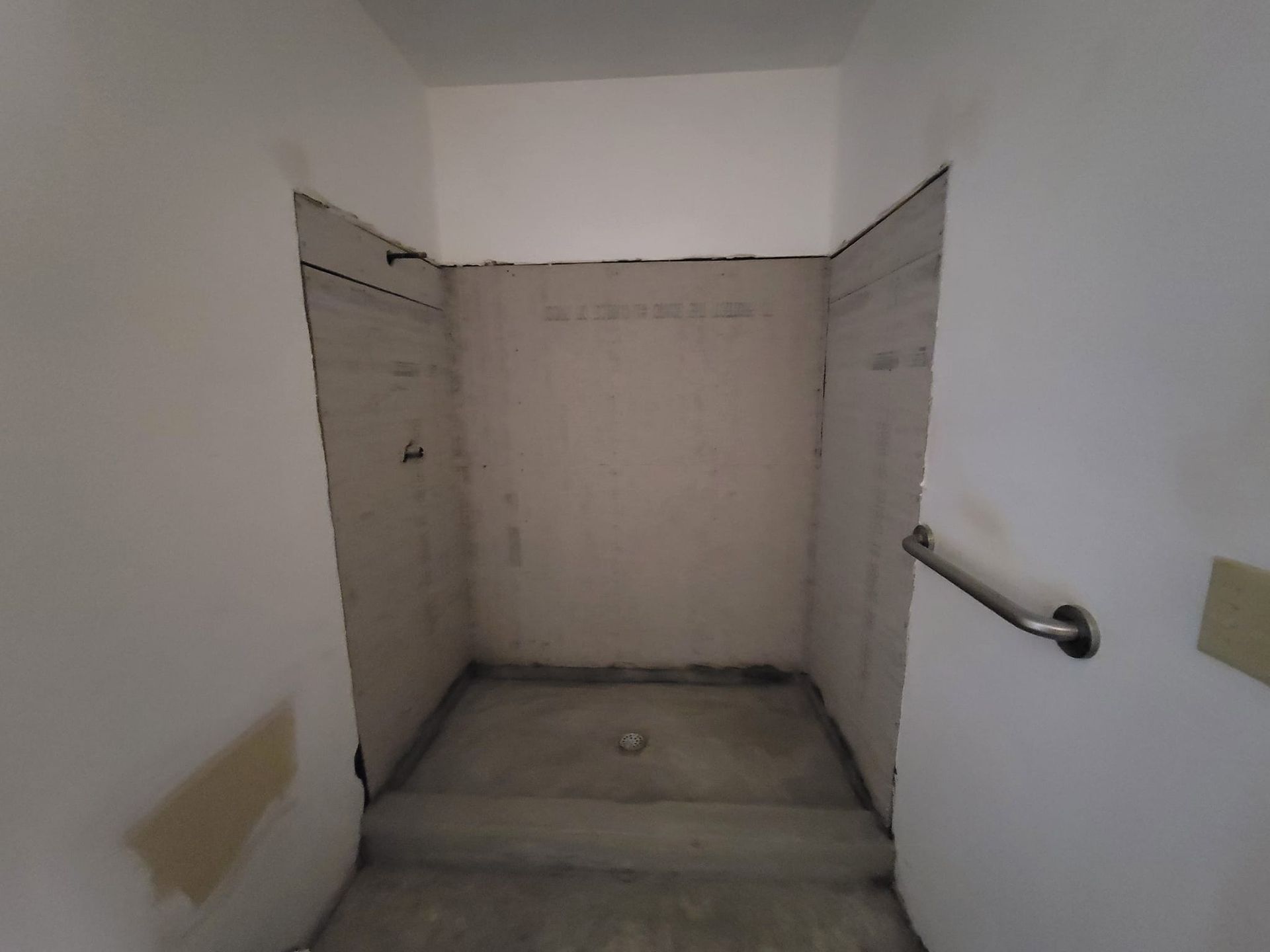 Empty shower stall with unfinished walls and concrete floor, viewed from the doorway. A grab bar is on the right wall.