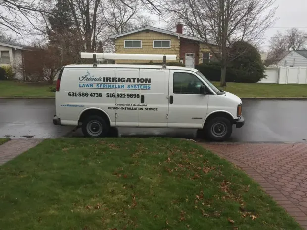 White van with "Talcott Irrigation" logo parked on a street in front of a house, carrying pipes on the roof.