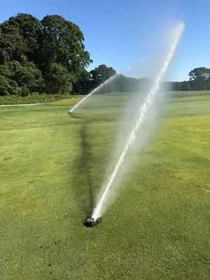 Sprinklers spraying water on a green golf course under a clear blue sky.