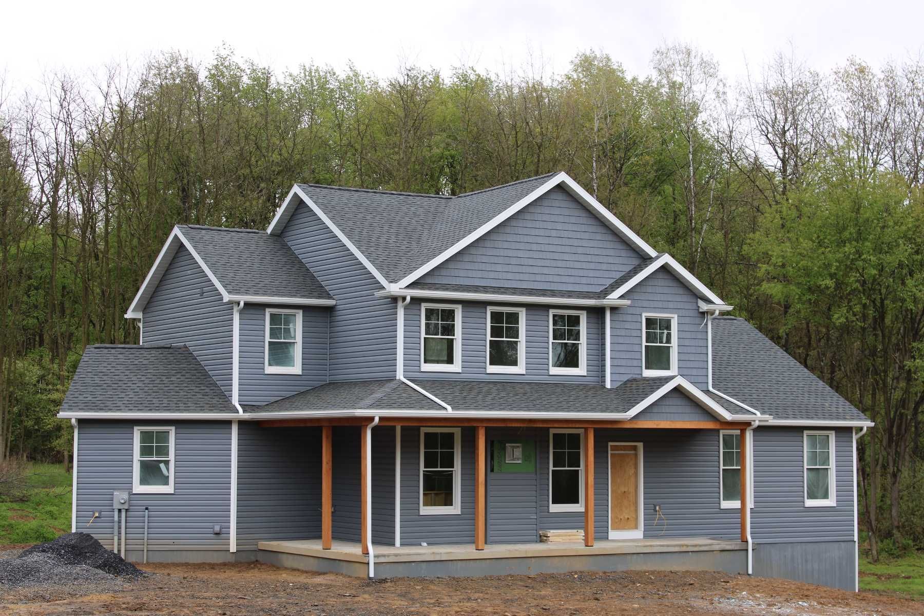 A large gray house with a porch and trees in the background.