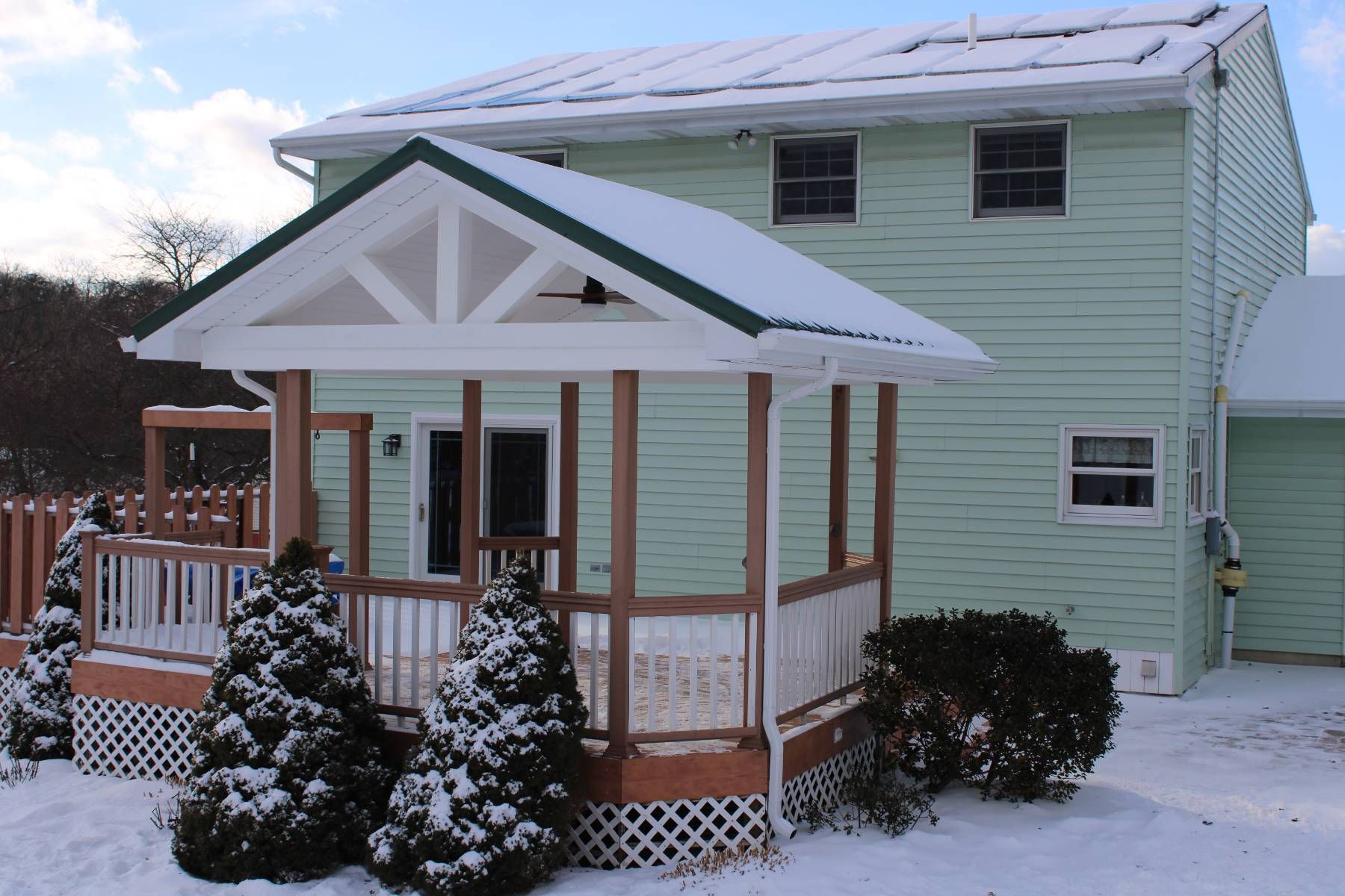 A green house with a porch covered in snow