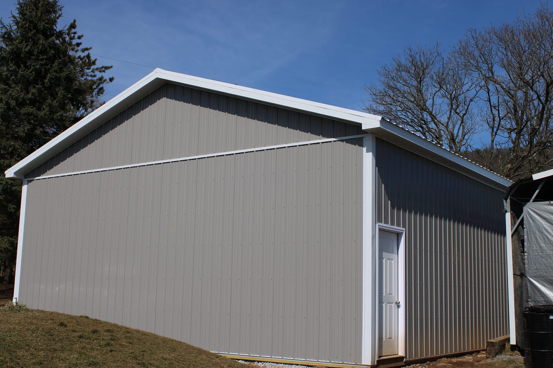 A large gray metal building with a white roof is sitting on top of a grassy hill.