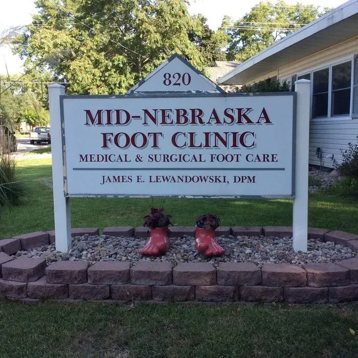 A sign for Mid-Nebraska Foot Clinic at 820, featuring two red, shoe-shaped planters, set in a stone garden bed on a lawn.