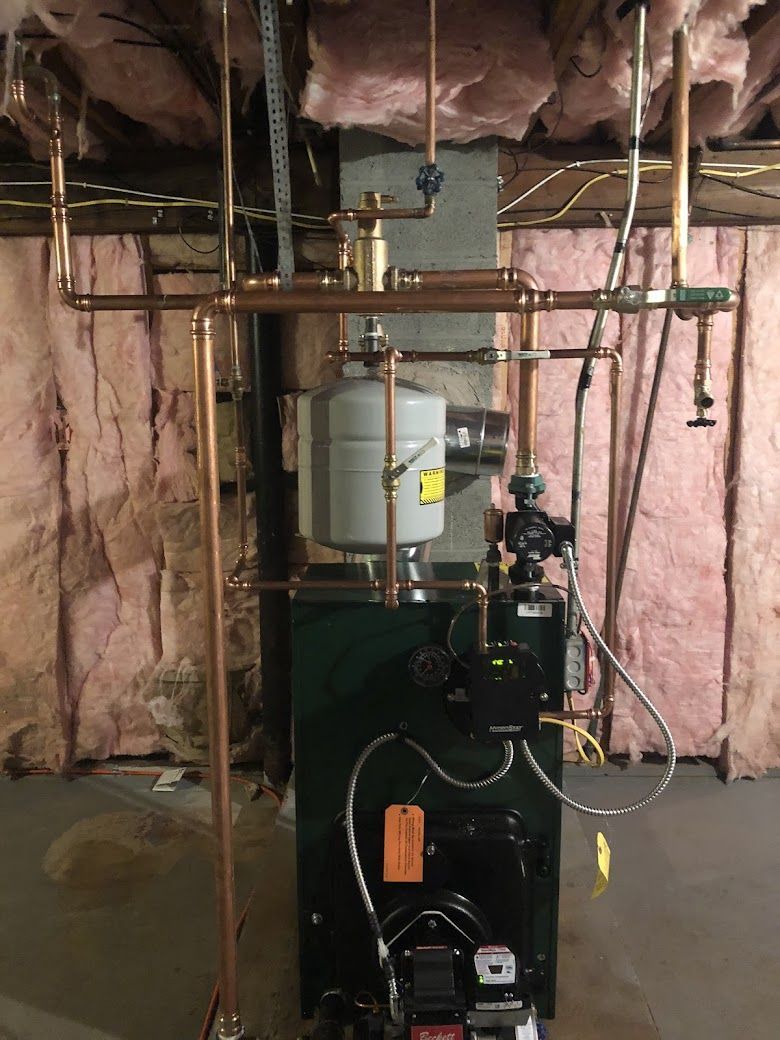 A green boiler is sitting in a basement with copper pipes.