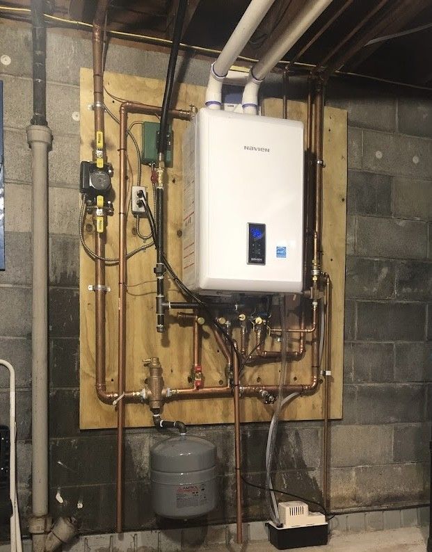A white water heater is mounted to a wall in a basement.