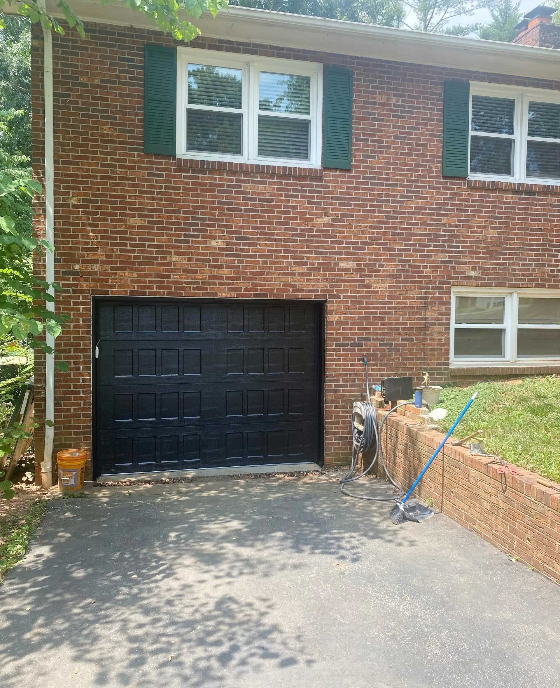Brick house with a black garage door, green shutters, and a driveway.