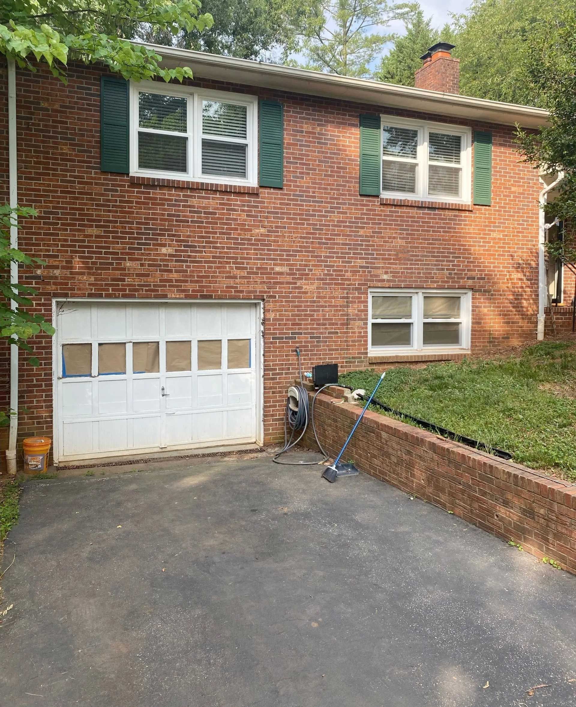 Brick house with a garage and two windows on the second floor, green shutters, and a driveway.