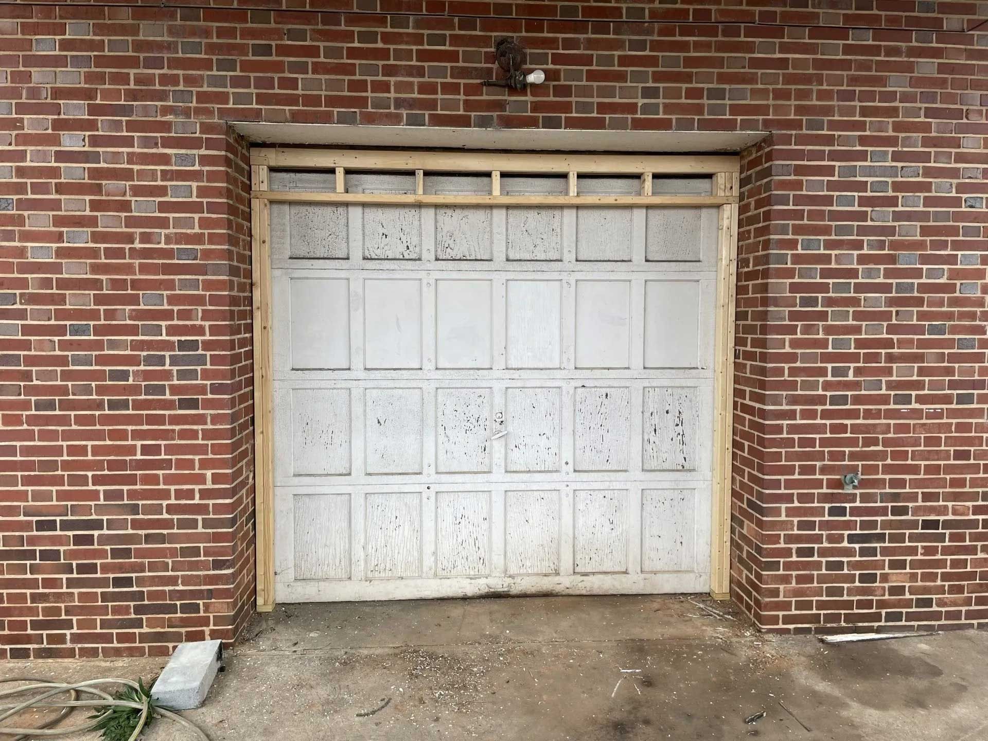 White garage door in a red brick building, with weathered surface and wood frame.