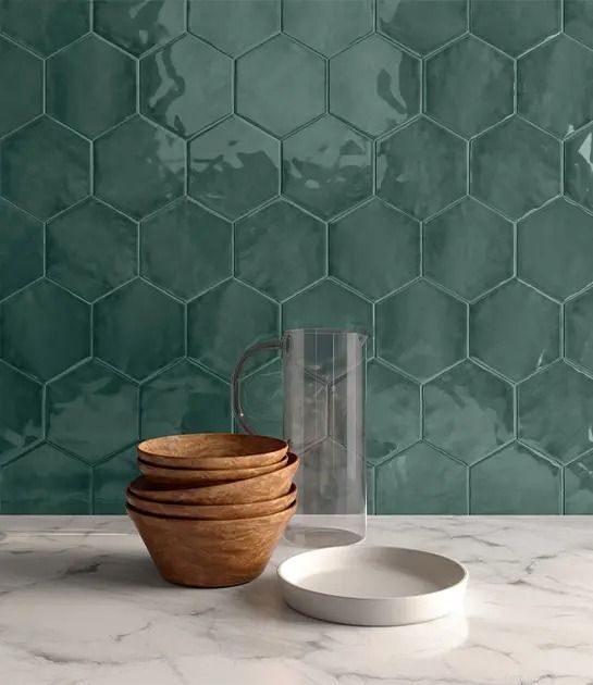 A stack of bowls , plates , and a pitcher on a counter in front of a green tile wall.