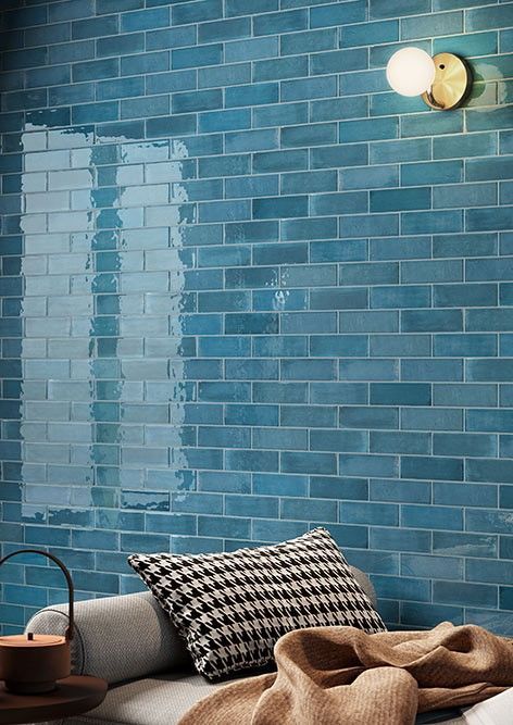 A bed with a blanket and pillows in front of a blue brick wall.