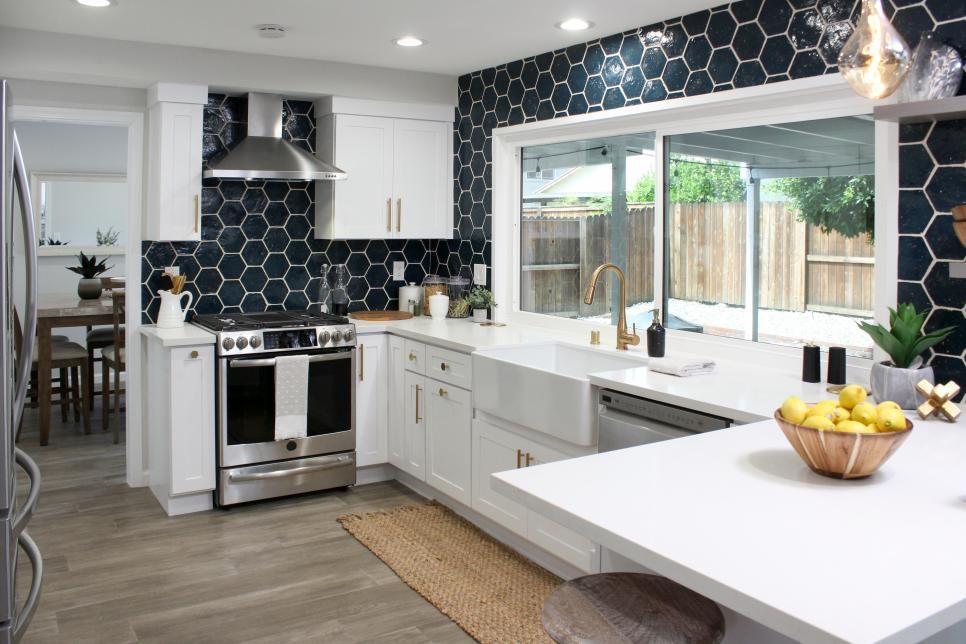 A kitchen with white cabinets , stainless steel appliances , a large window and a bowl of lemons on the counter.