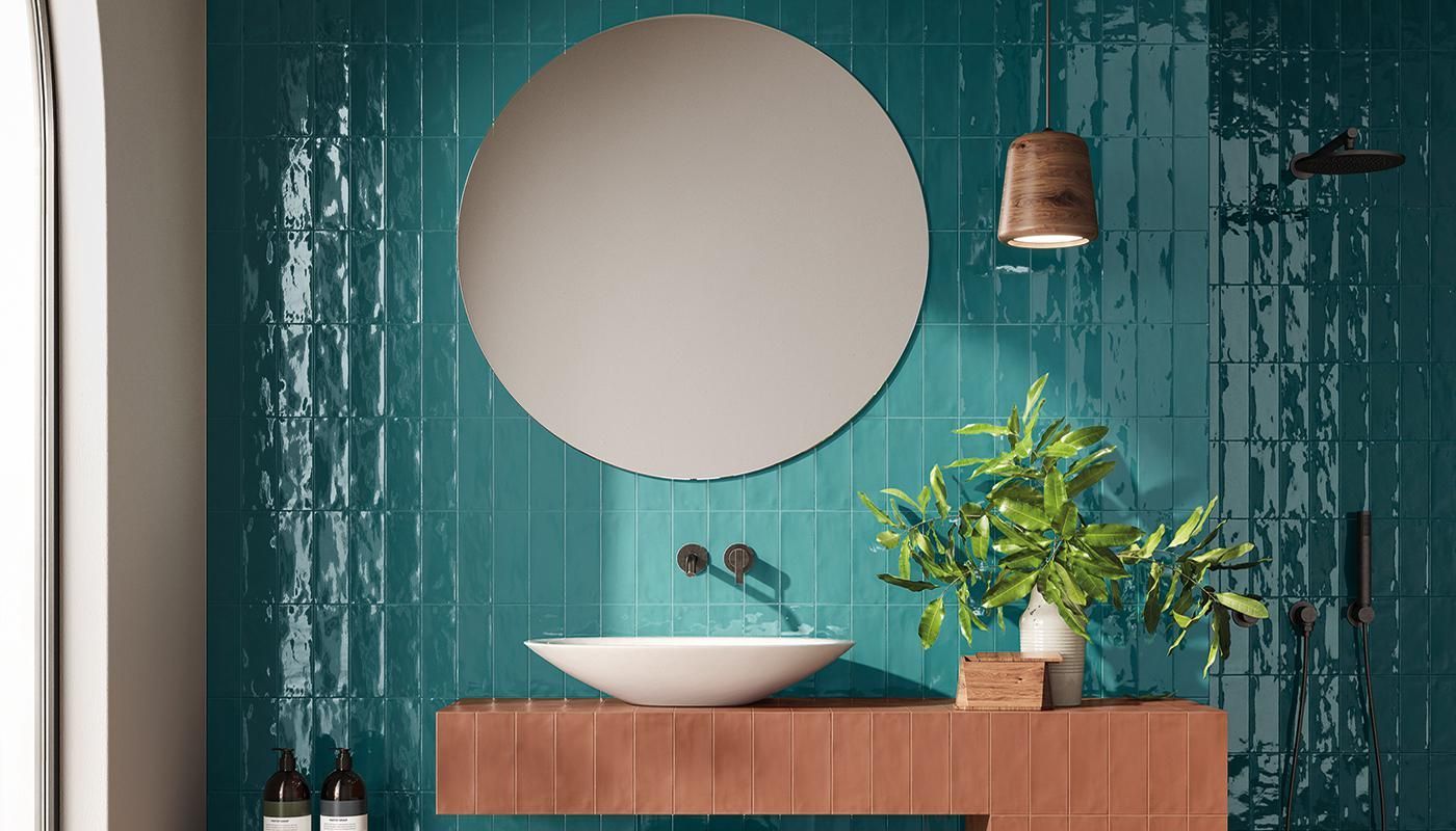 A bathroom with blue tiles , a sink , a mirror and a plant.