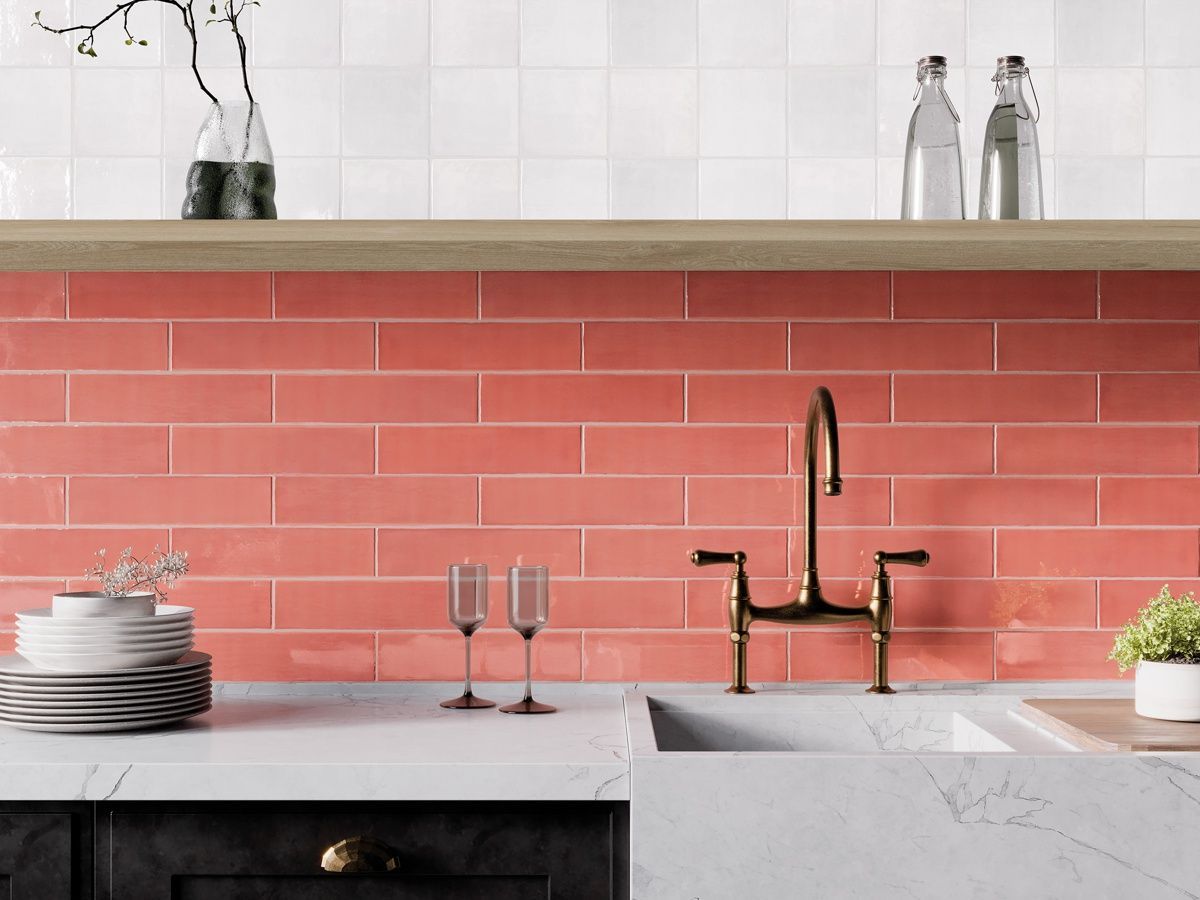 A kitchen with red tiles , a sink , a faucet and a shelf.