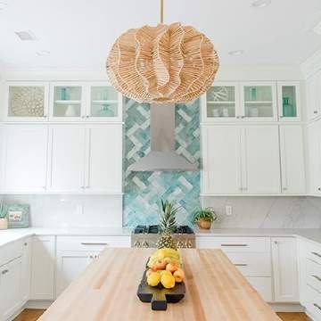 A kitchen with white cabinets , a wooden table , a stove and a wicker pendant light.