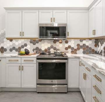 A kitchen with white cabinets , stainless steel appliances , and hexagonal tiles on the wall.