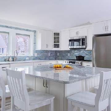 A kitchen with white cabinets , granite counter tops , stainless steel appliances and a large island.