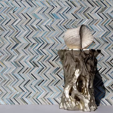 A vase sitting on top of a tree stump in front of a chevron tile wall.