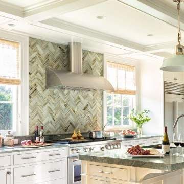 A kitchen with white cabinets , a stove , a sink and a hood.