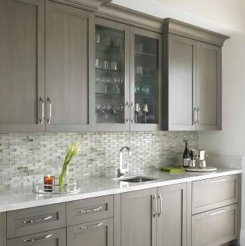 A kitchen with gray cabinets , white counter tops , and a sink.